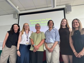 Six women look into a camera smiling in a university teaching room